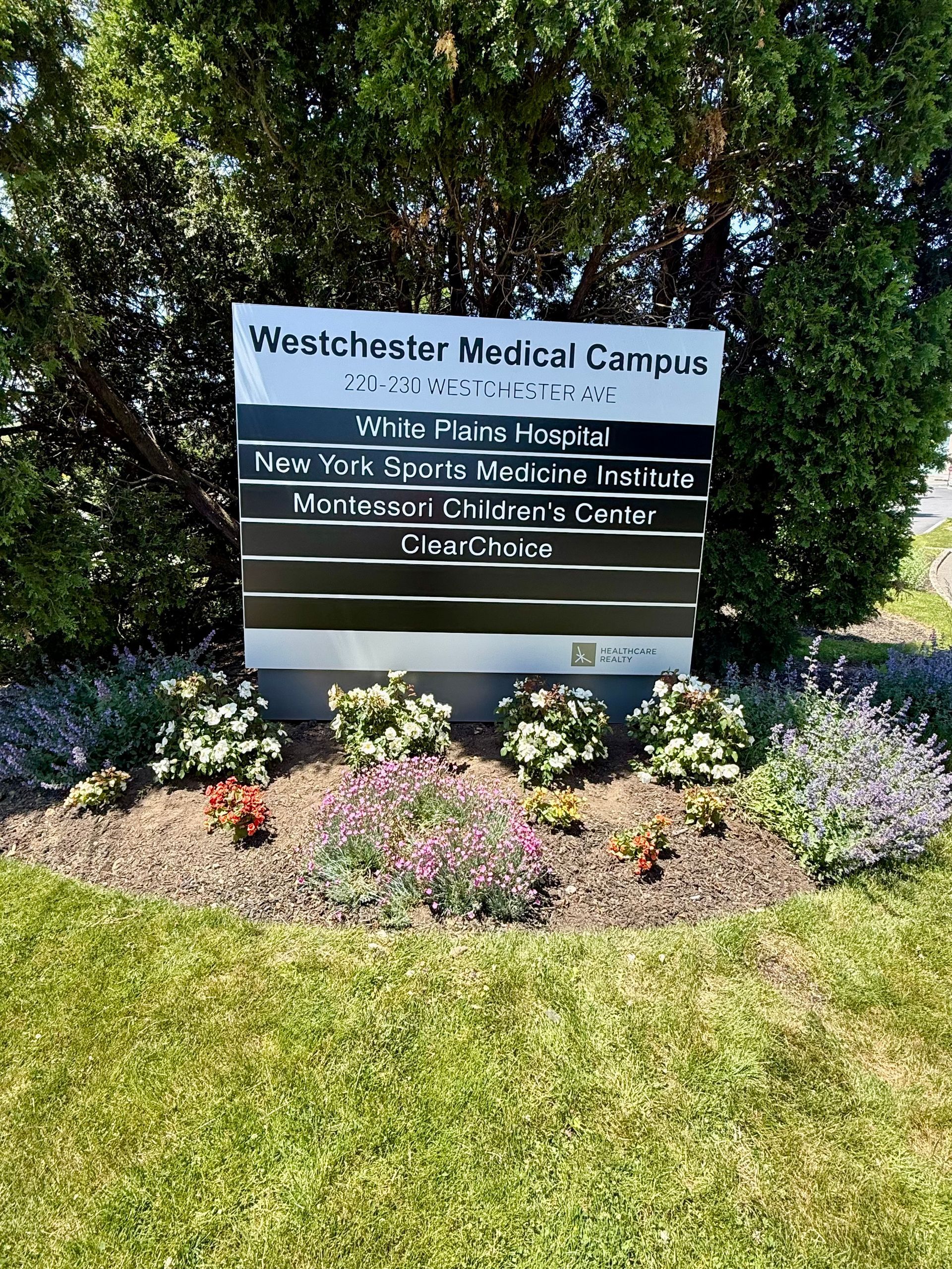 Westchester Medical Campus sign amid greenery and flowers in front of a grassy lawn