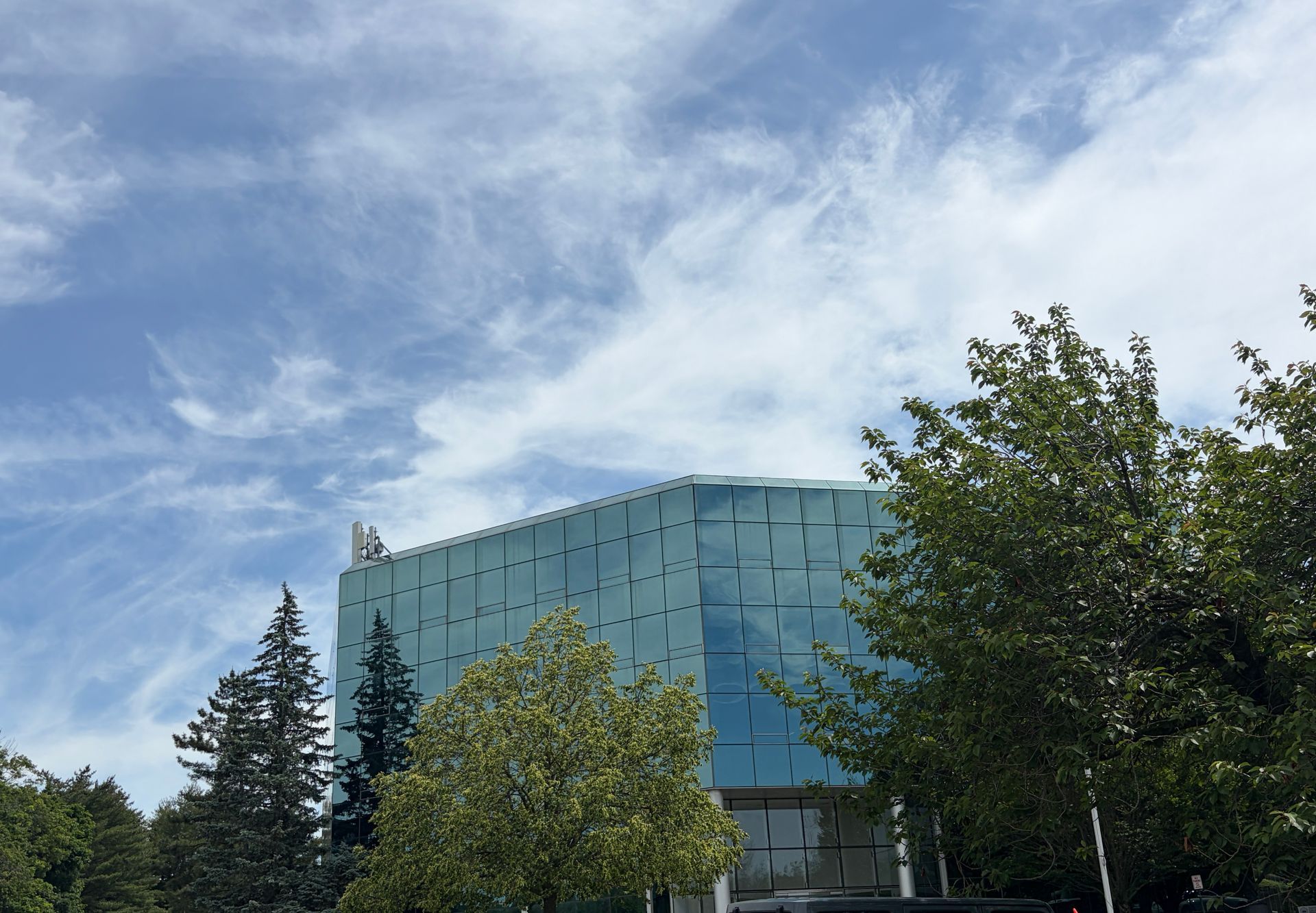 Blue glass building behind trees under a partly cloudy sky