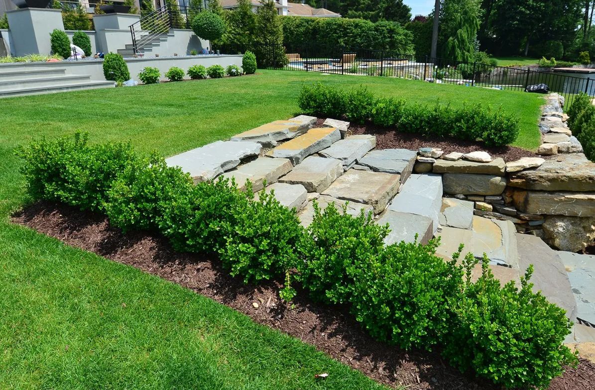 Lush green lawn with manicured hedges and stone steps leading down to the water's edge.