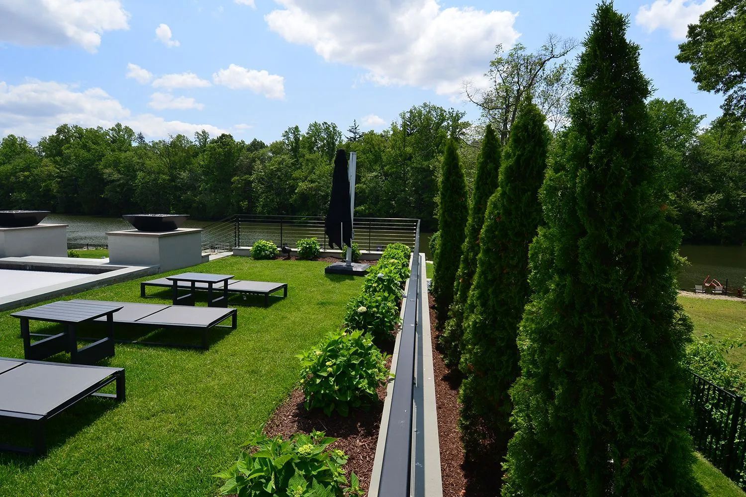 Lawn chairs on a grassy rooftop overlooking a river, with tall green trees and a blue sky.