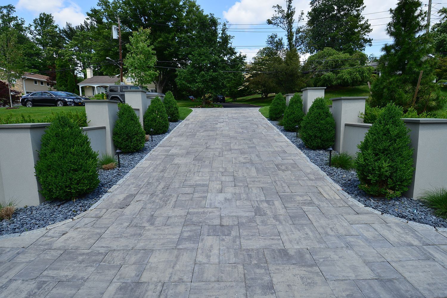 paver driveway lined with small trees, leading to a house