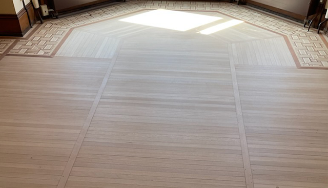 Light-colored wooden floor with decorative border. Sunlight streams in from the top.