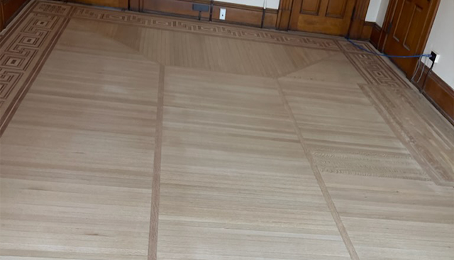 Light wood floor with inlaid border and vertical lines.