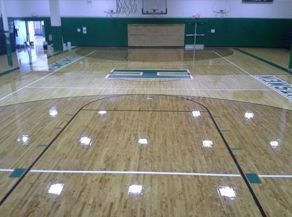 Empty basketball court with polished wooden floor and green accents.