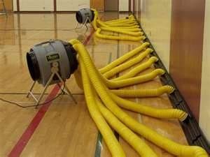 Two fans with yellow hoses drying a wooden floor.