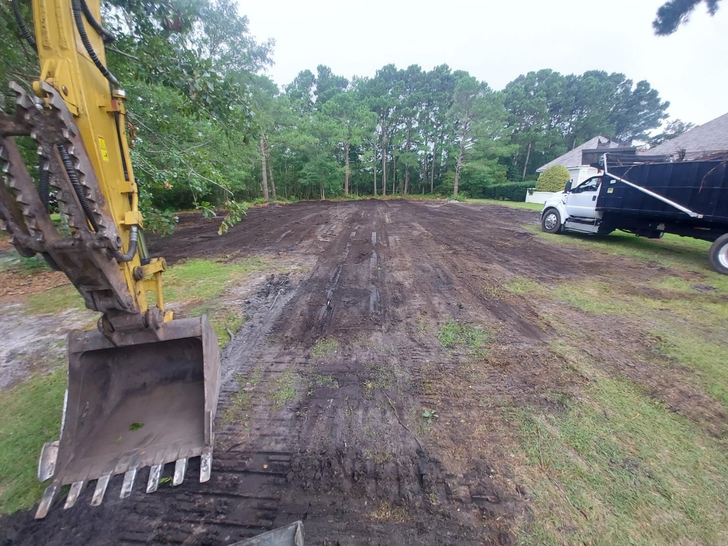 A yellow excavator is digging a dirt road next to a dump truck.