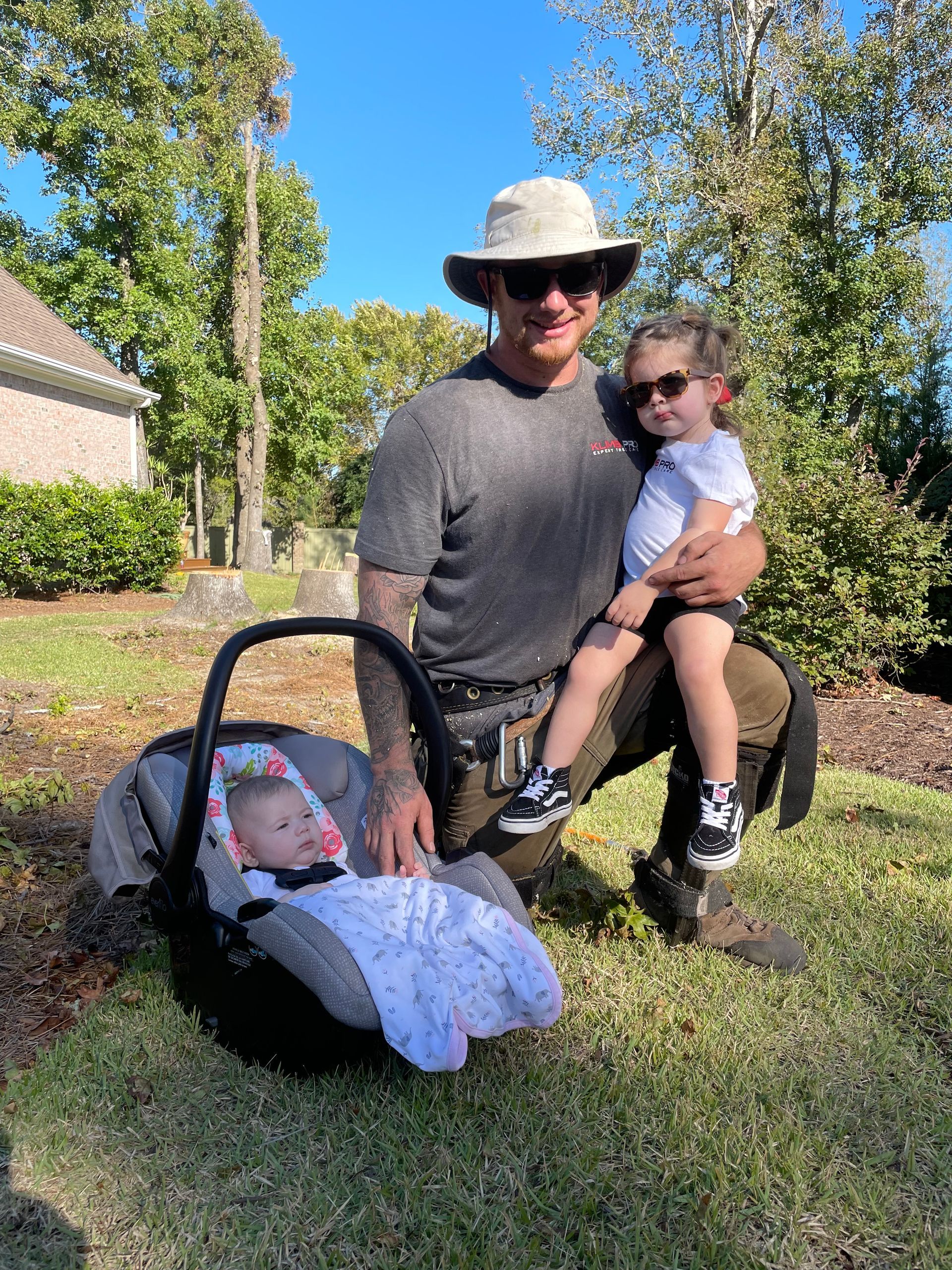 A man is kneeling down in the grass holding a baby in a car seat.