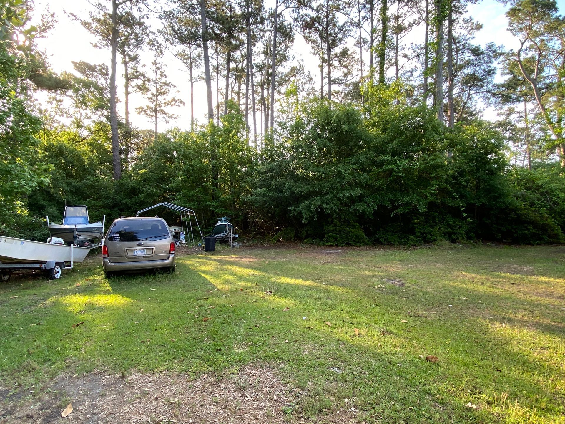 A car is parked in a grassy field with trees in the background.