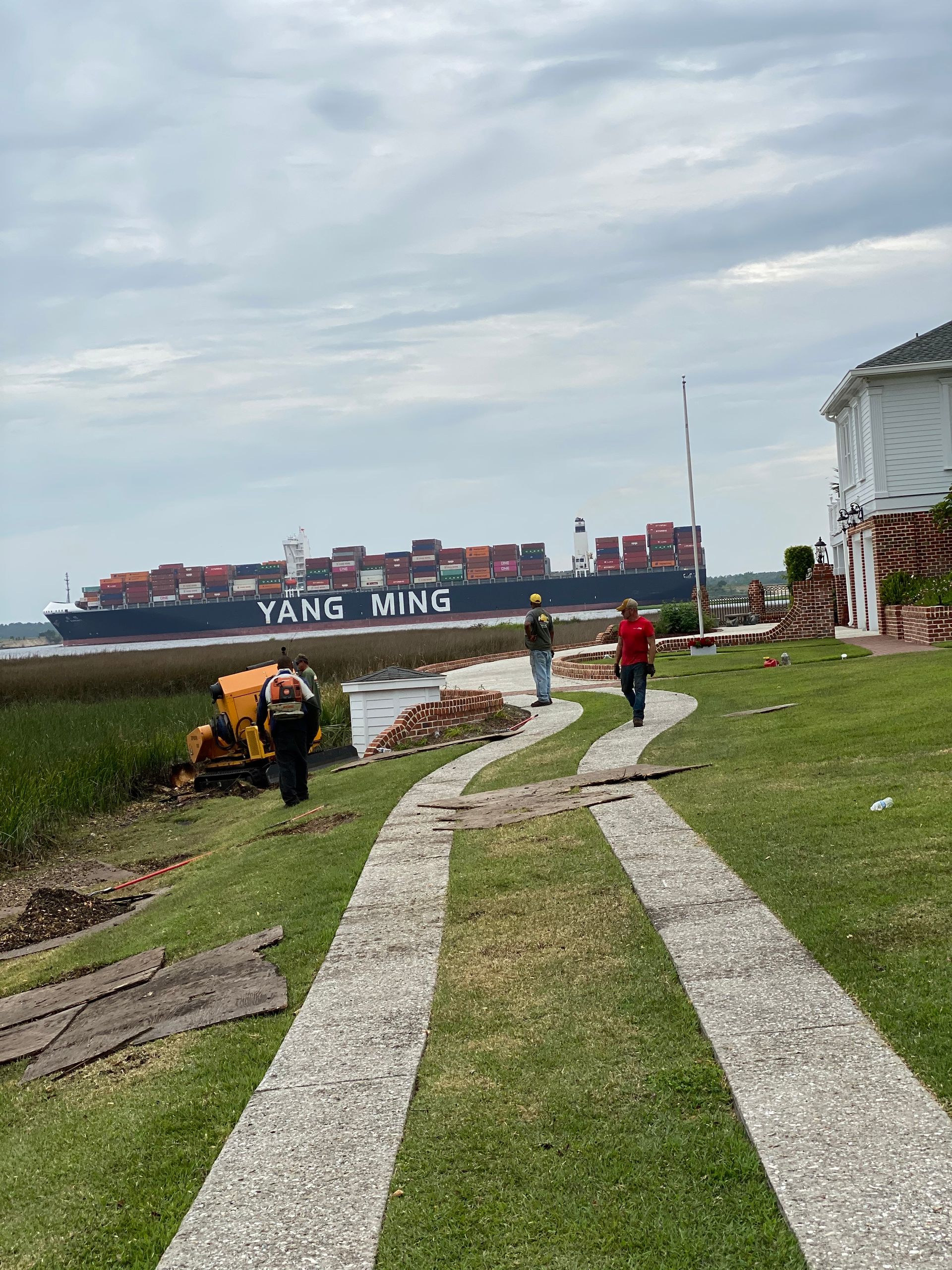 A couple of people walking down a path next to a large ship.