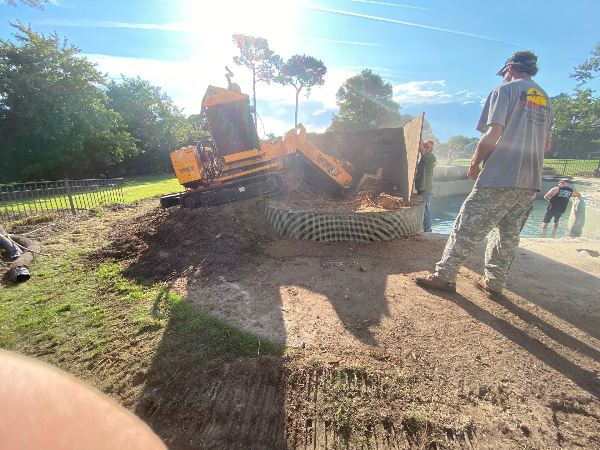 A man is standing next to a machine that is cutting a tree stump.