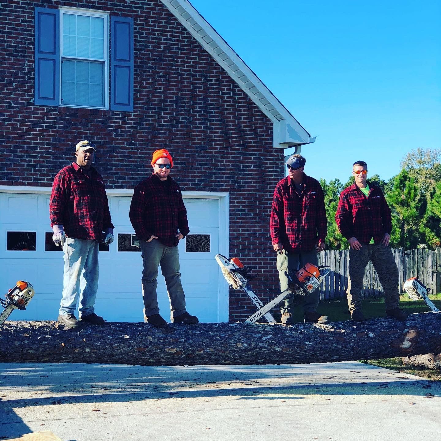 A group of men standing next to a large log in front of a brick house