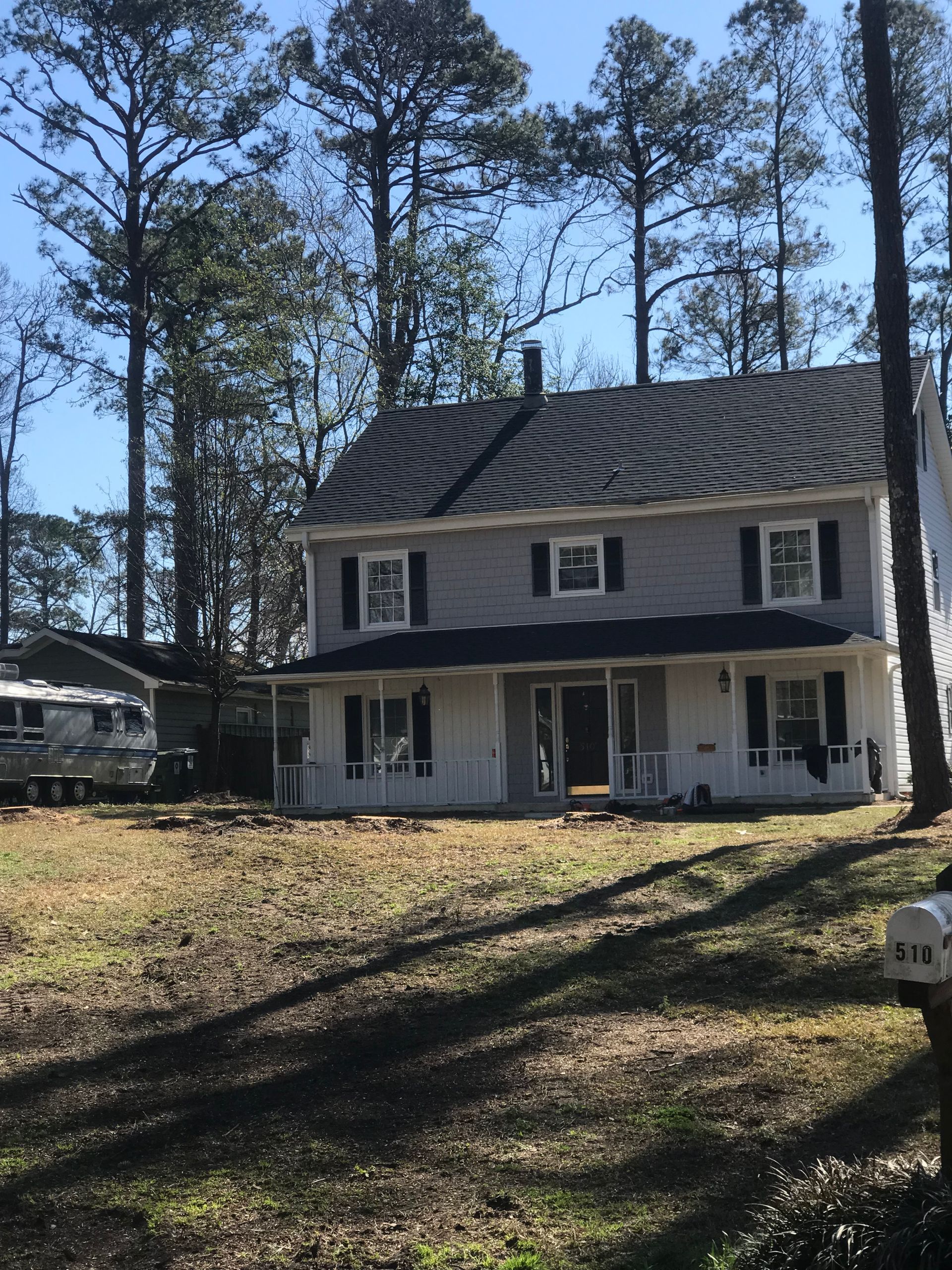 A white house with black shutters is surrounded by trees