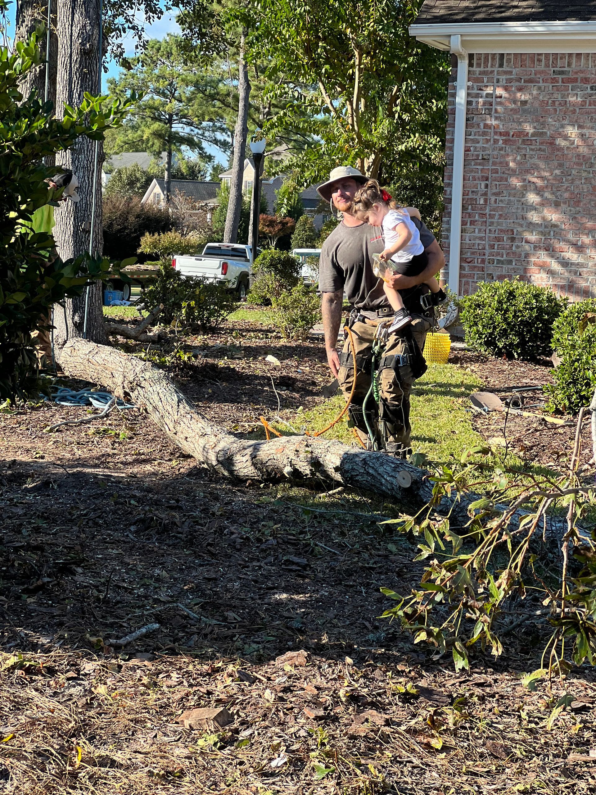 A man is holding a baby in his arms while standing next to a tree.