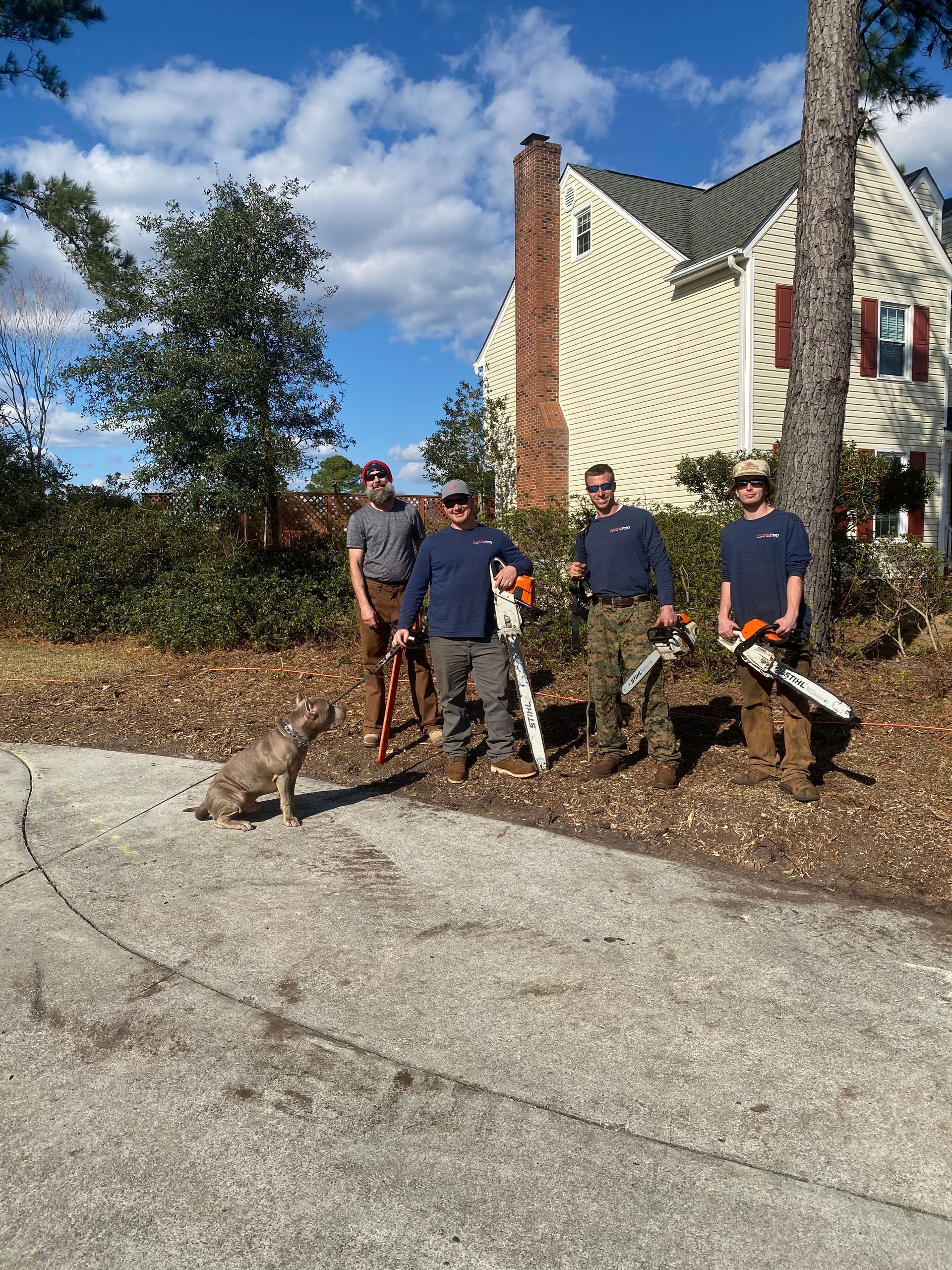 A group of men are standing in front of a house holding chainsaws.