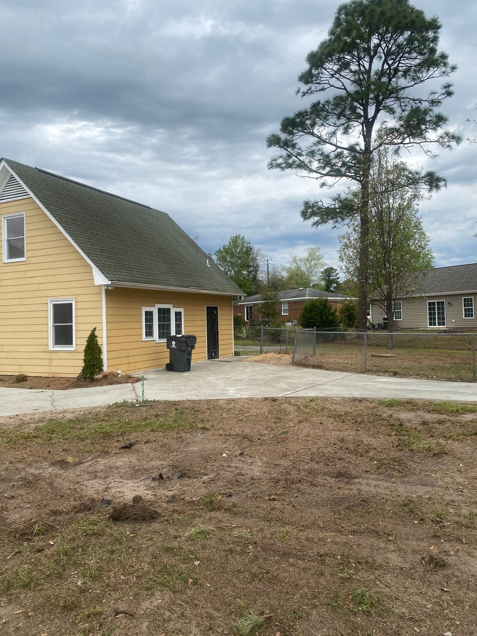 A yellow house with a green roof is sitting in the middle of a dirt field.