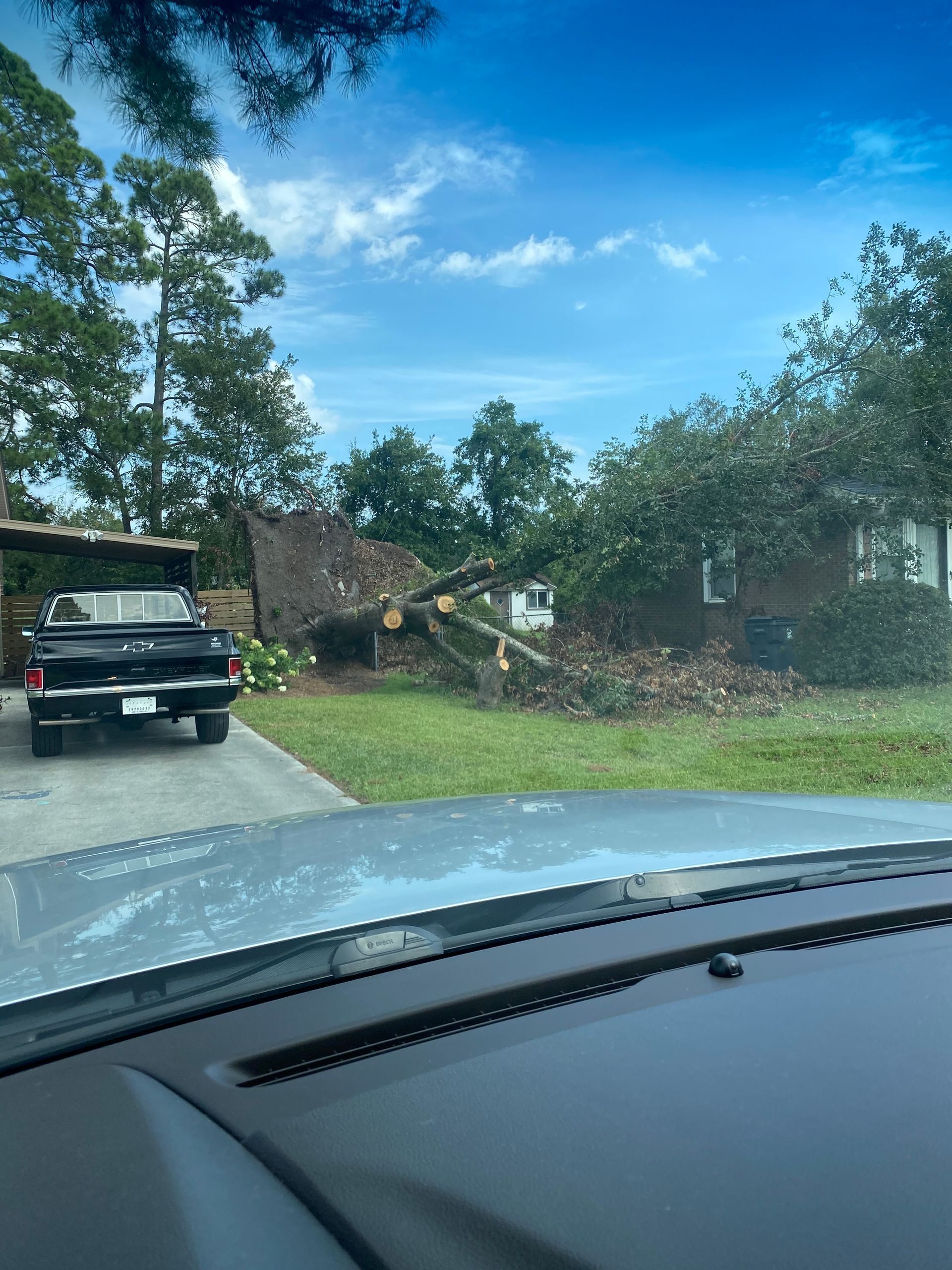 A truck is parked in front of a house that has been damaged by a tree.