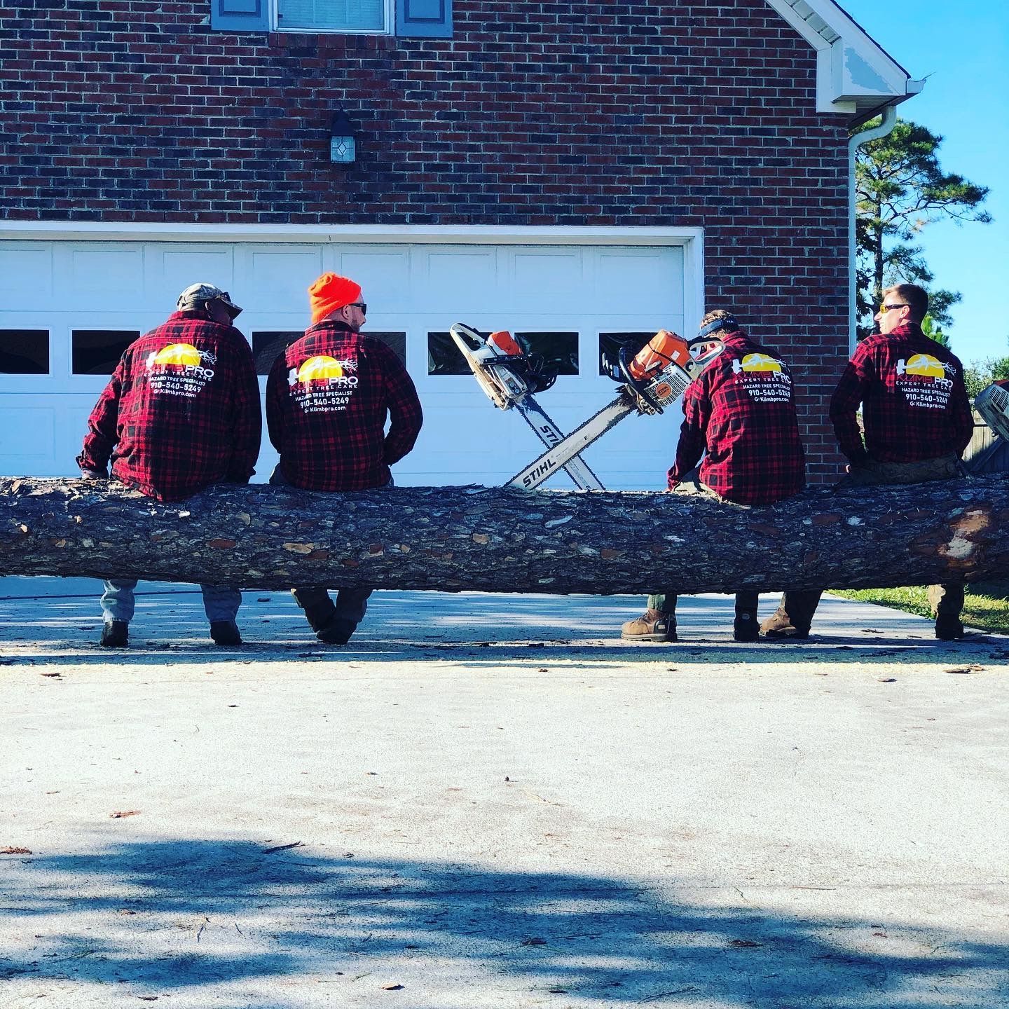 A group of men are sitting on a large log in front of a garage