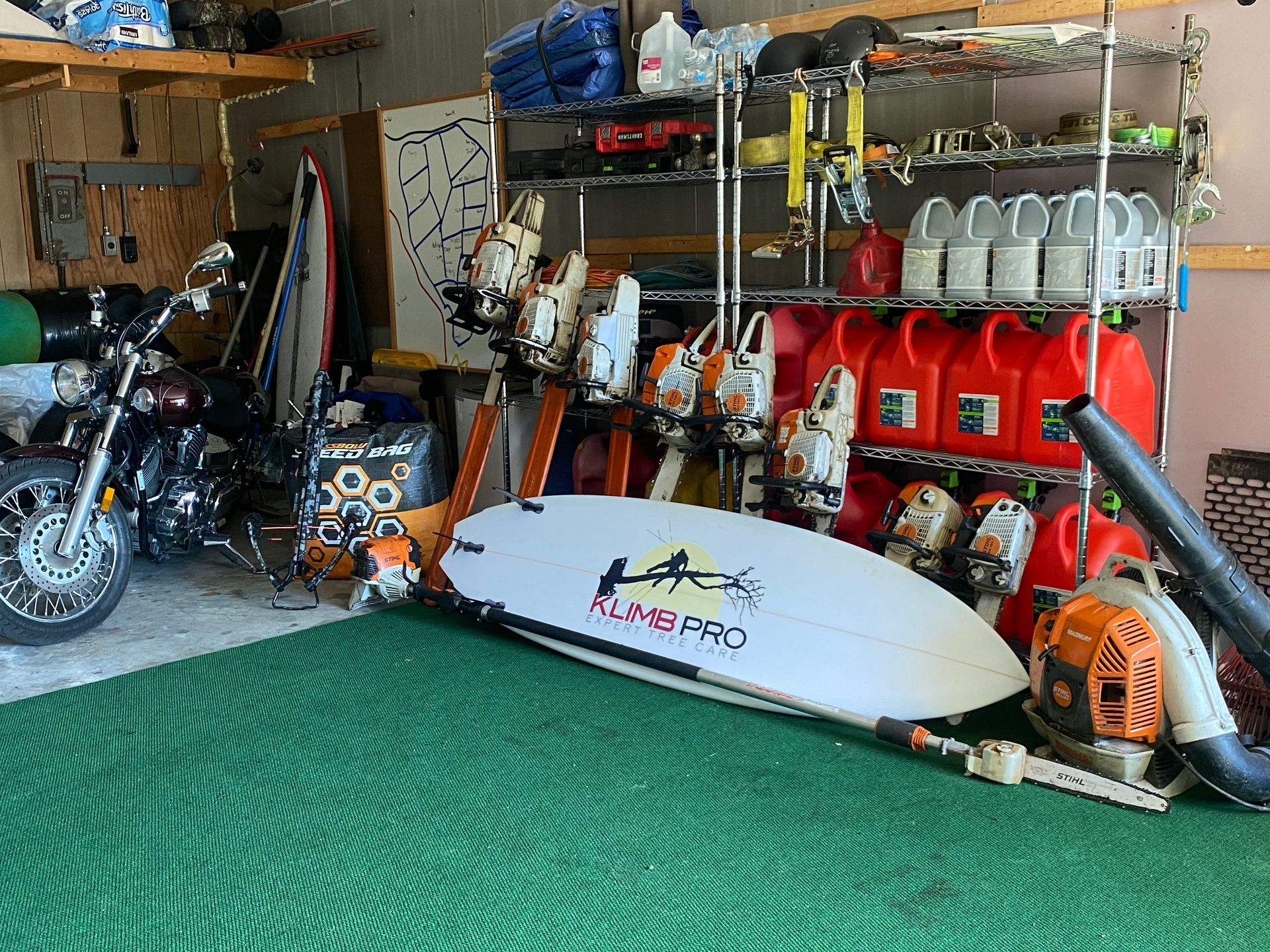 A motorcycle is parked in a garage next to a surfboard.