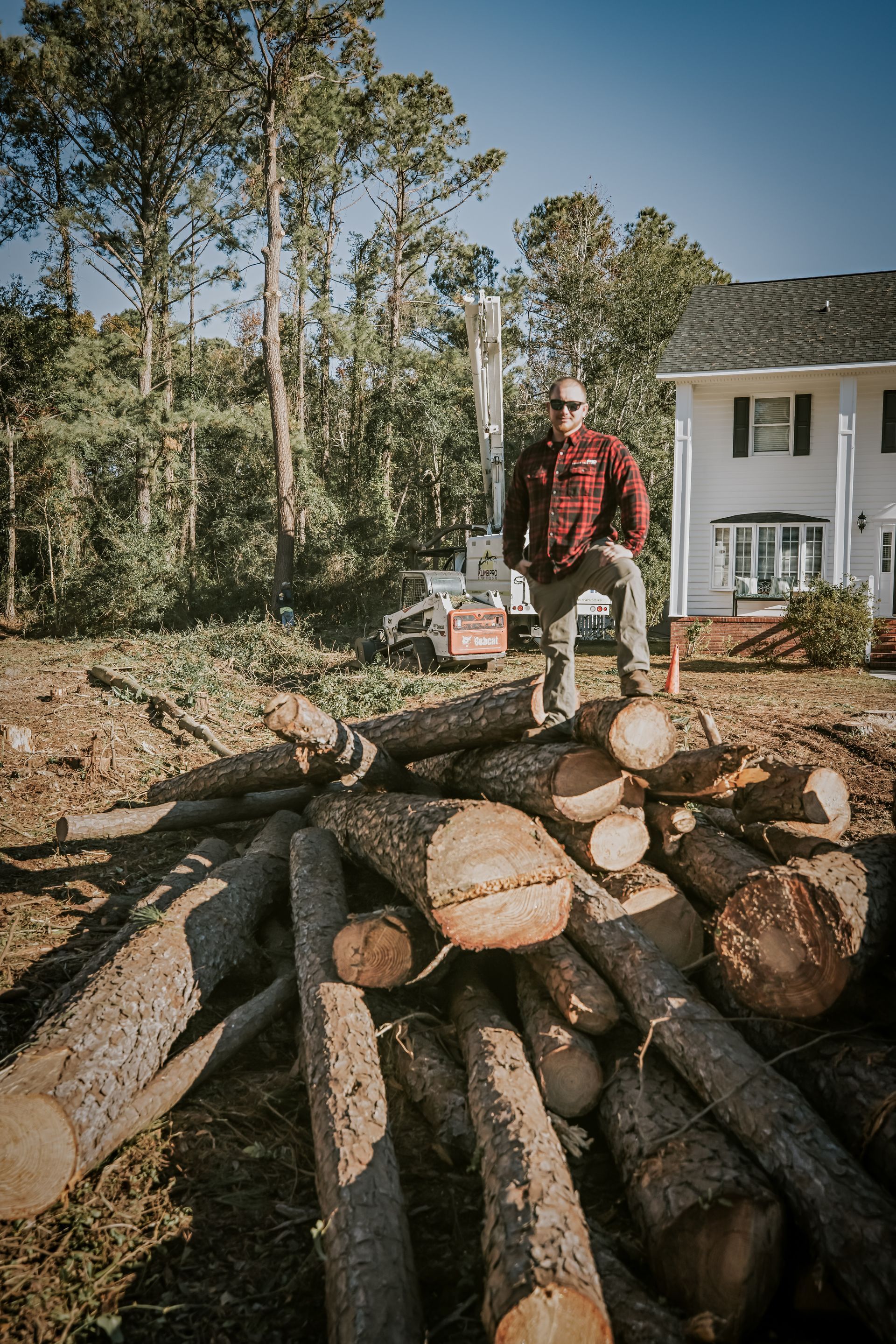 A man is sitting on a pile of logs in front of a house.