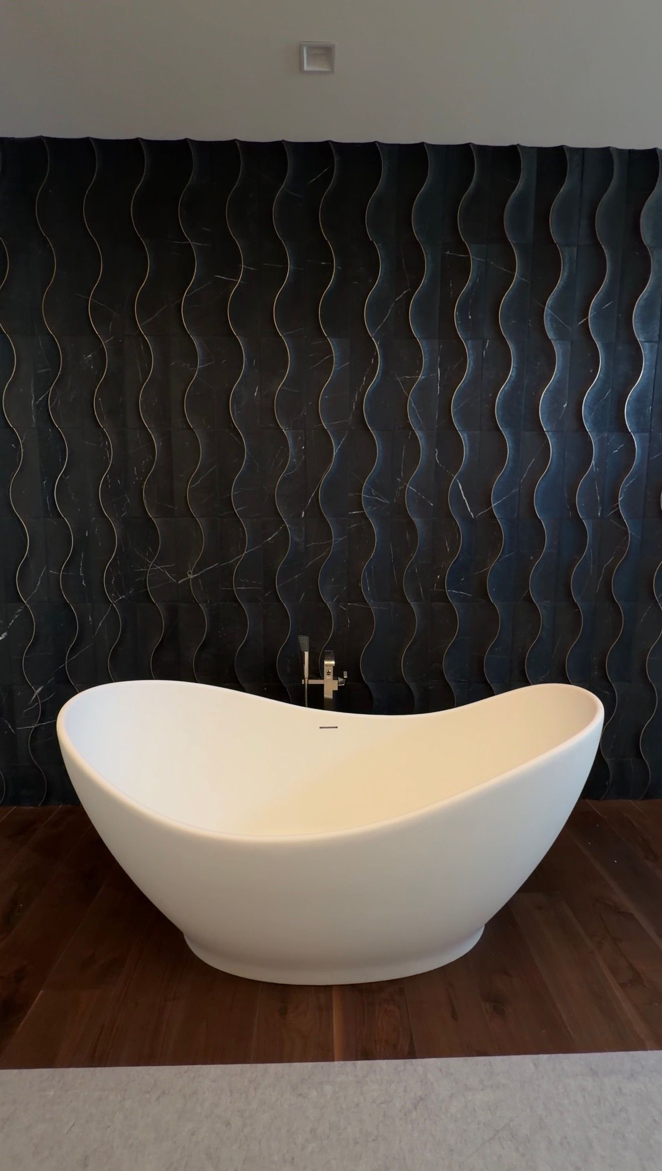White freestanding bathtub against a dark textured wall in a modern bathroom