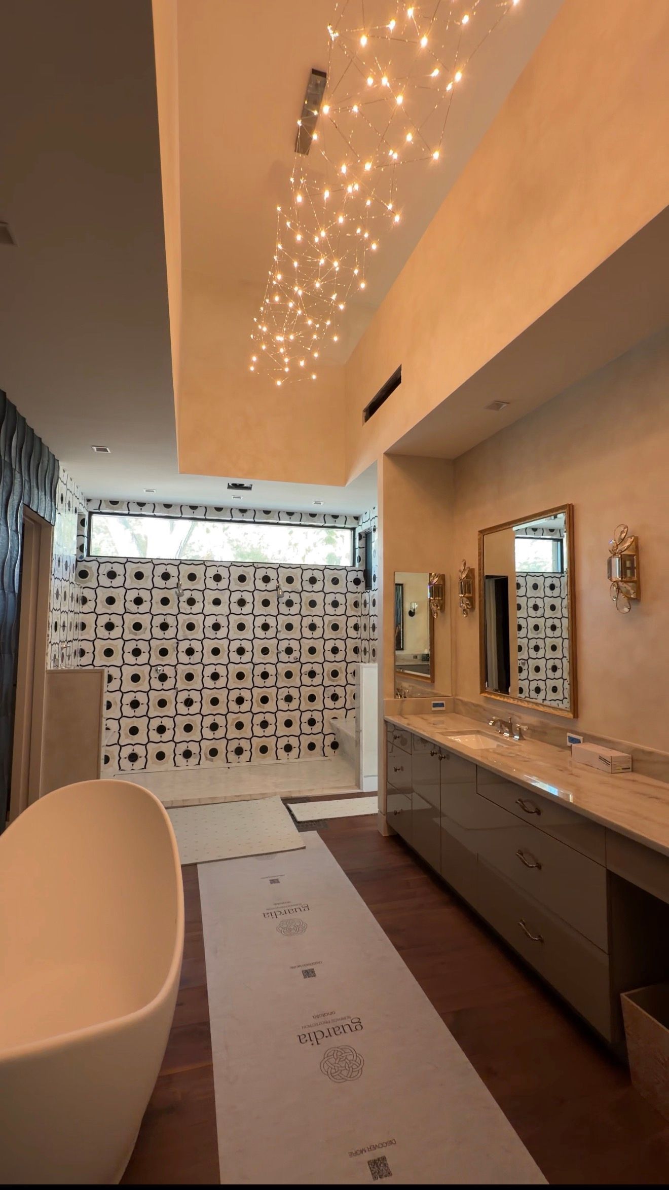 Modern bathroom with a long vanity, white tub, tiled shower wall, and warm ceiling lights