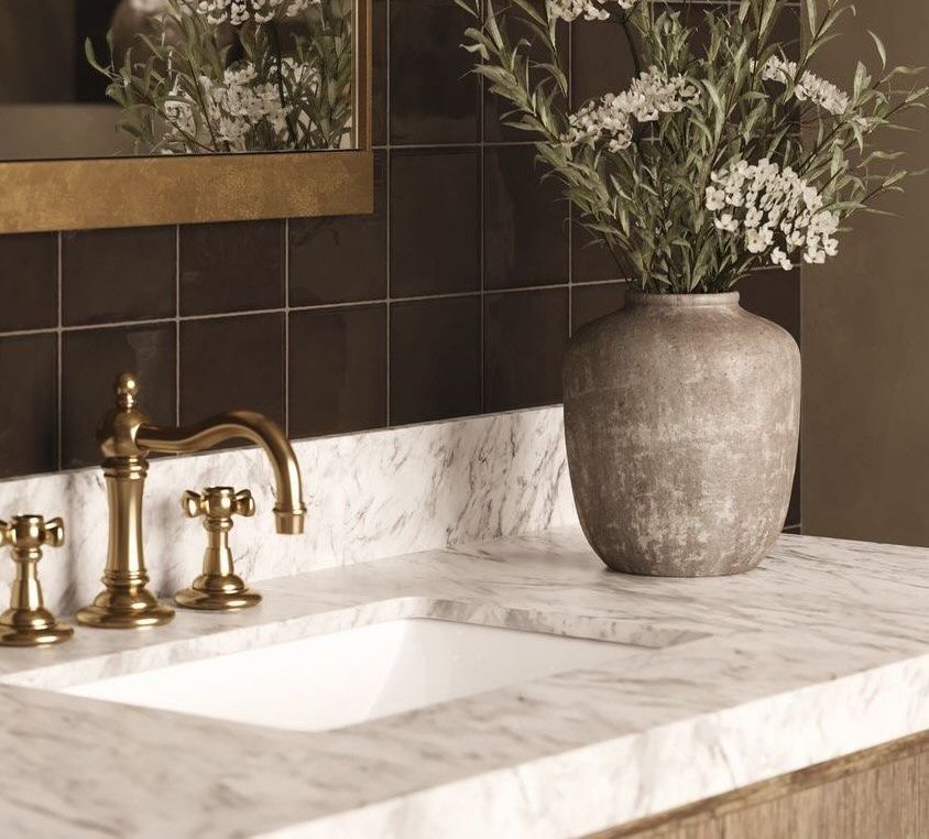 Bathroom vanity with gold faucet, marble countertop, and decorative vase of flowers.
