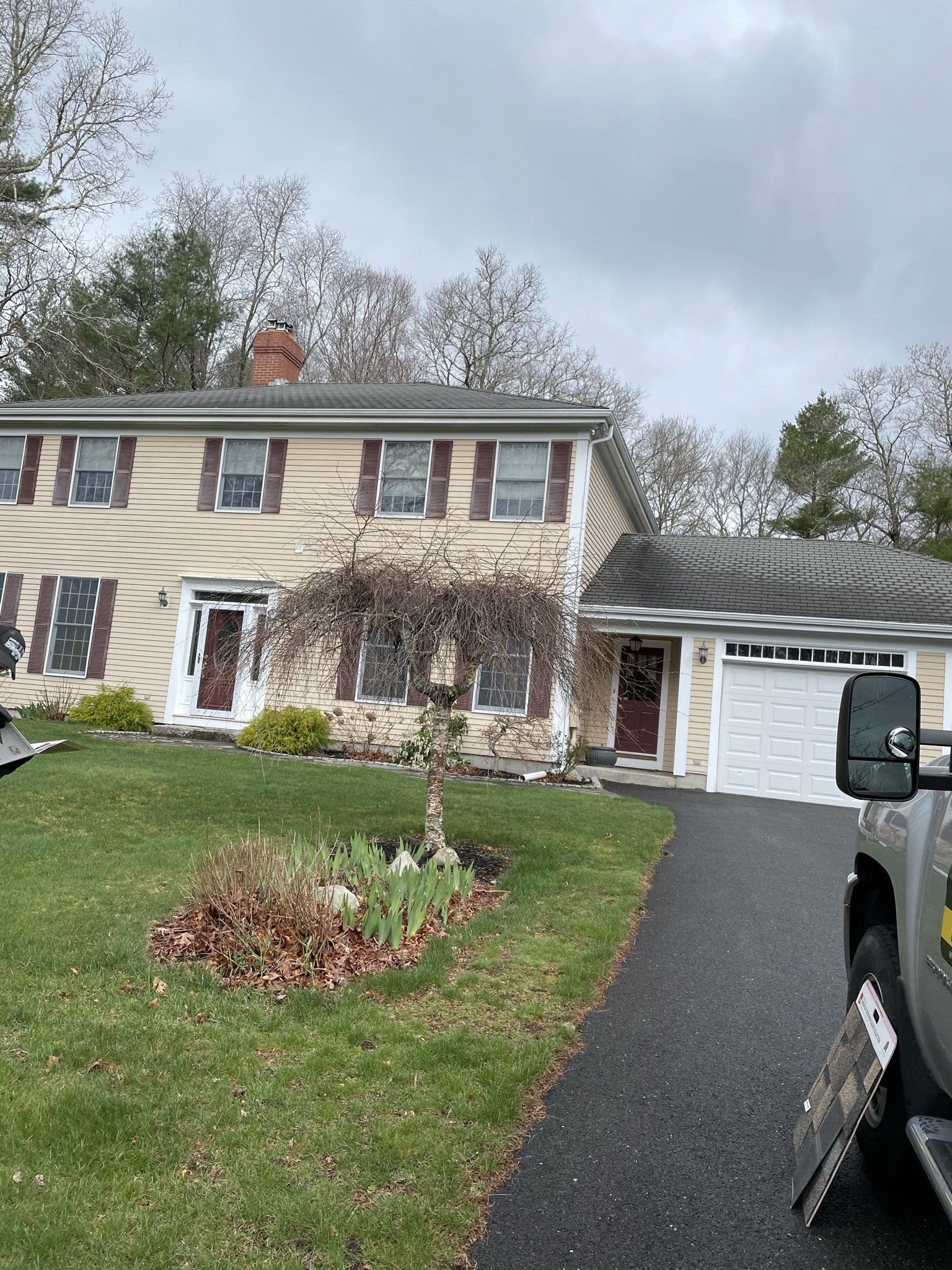 Two-story beige house with brown shutters, a dark driveway, and a truck in the foreground.