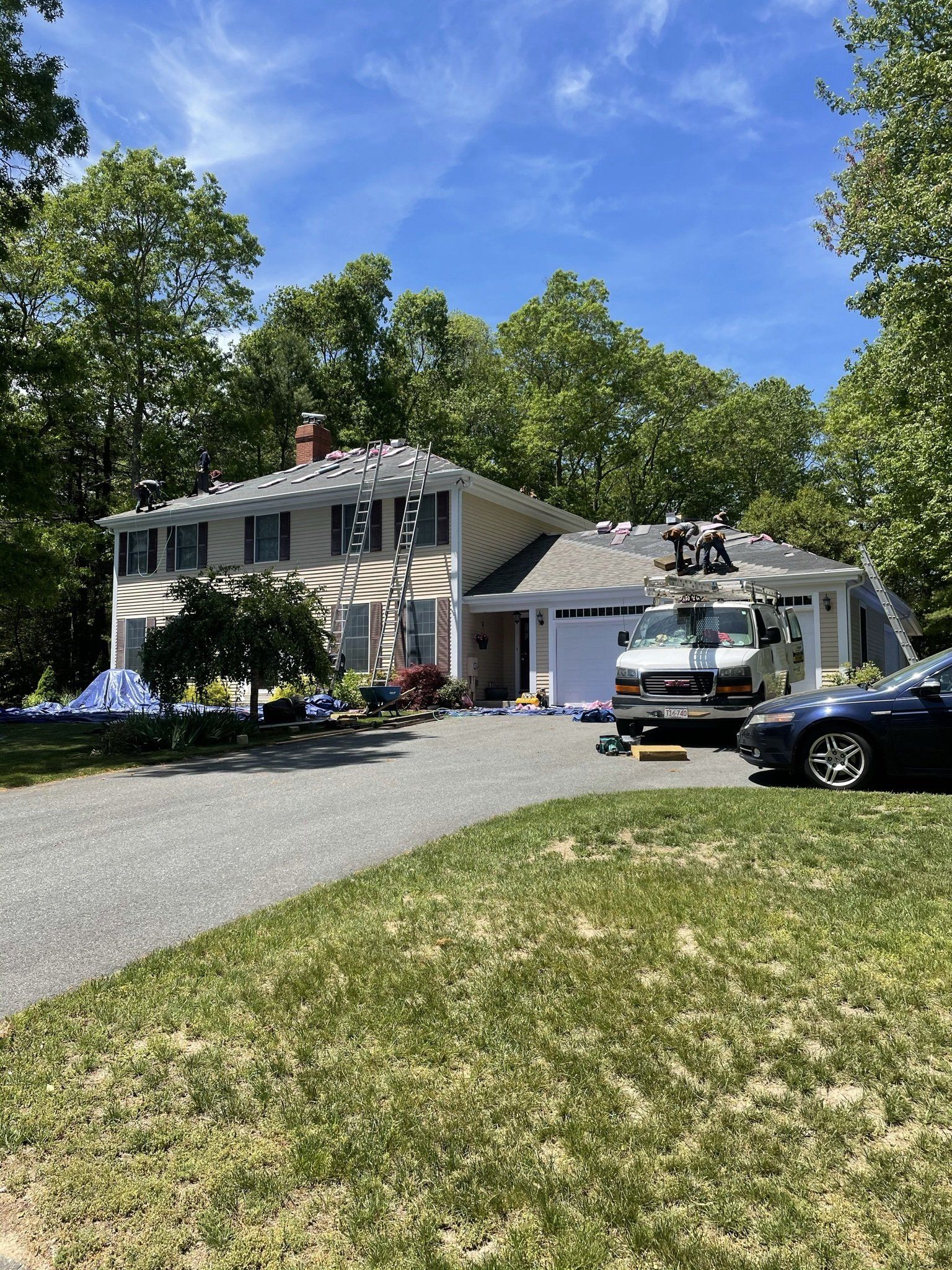 House with a roof replacement in progress; workers on the roof, truck parked in the driveway.