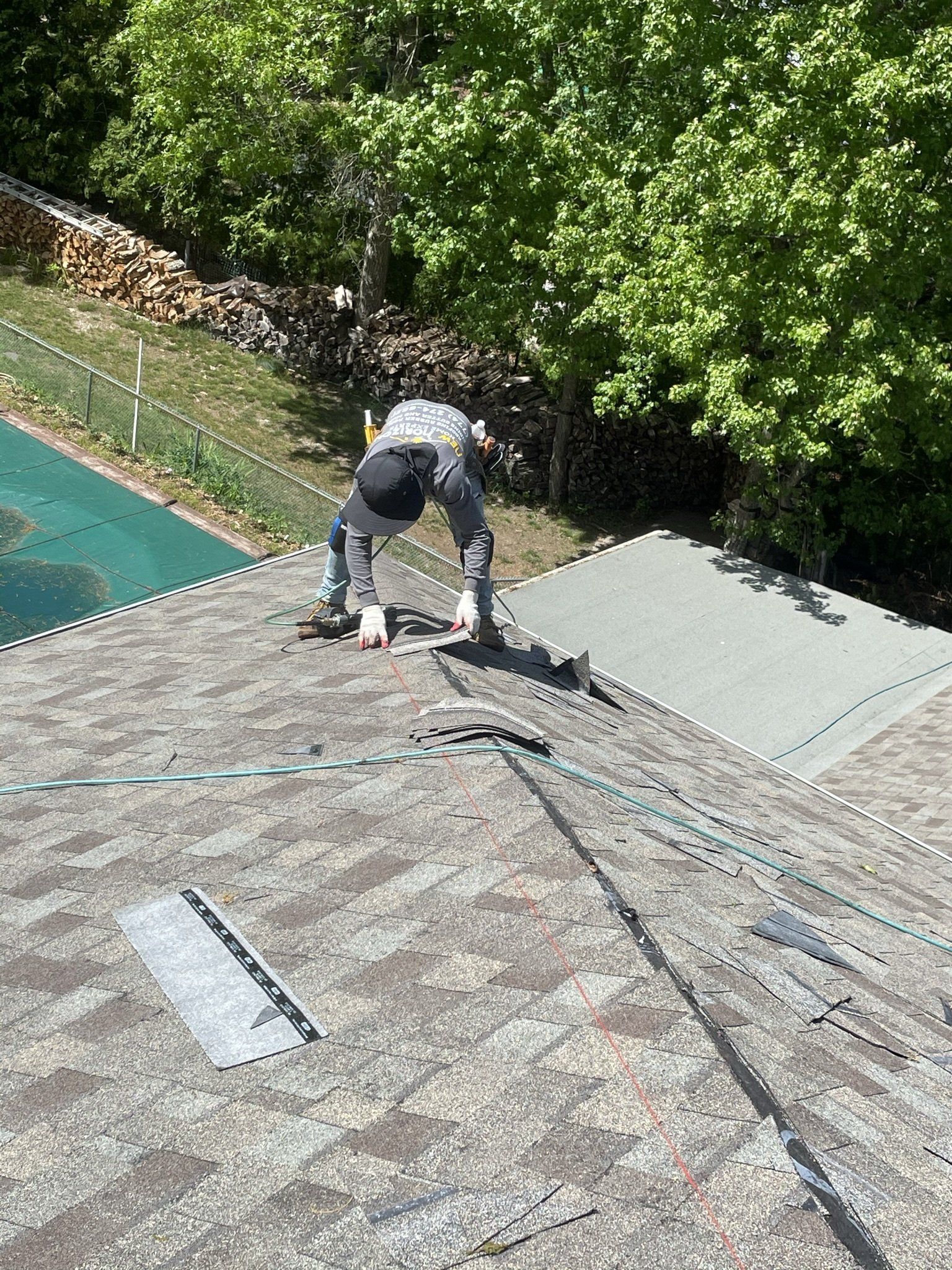 Person on a roof, hunched over, working. Green trees in the background.