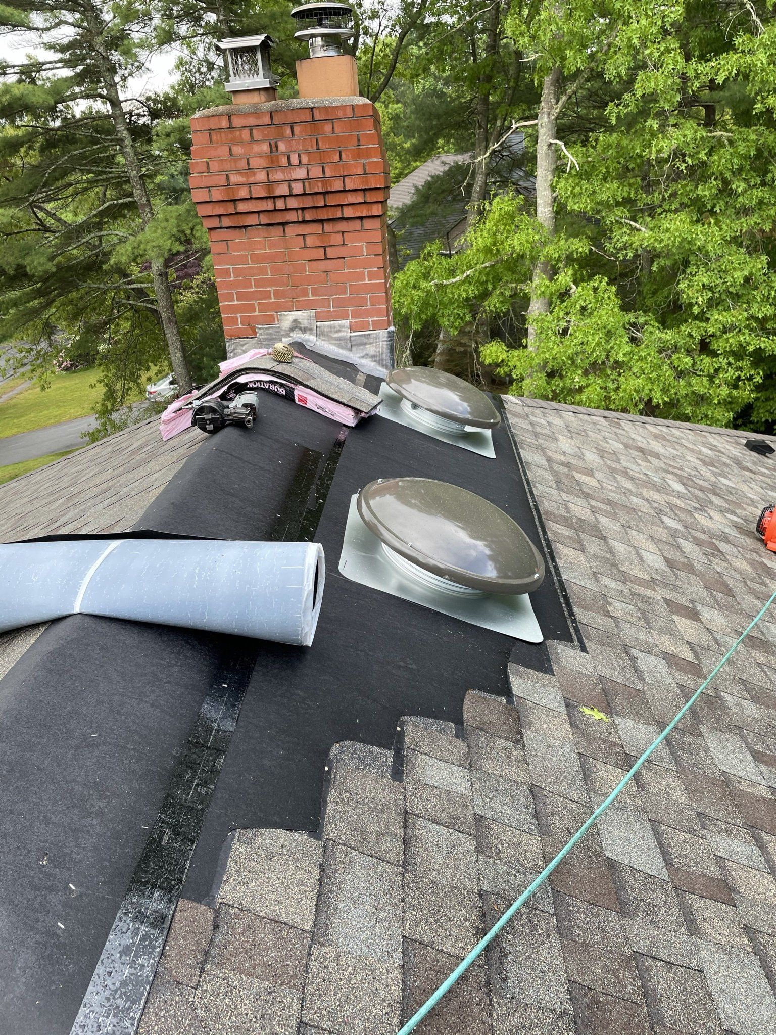 Roofer installing asphalt shingles and skylight. Chimney and trees in the background.