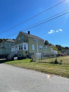 Two-story light green house with a grassy yard on a sunny day. Power lines and a blue sky.