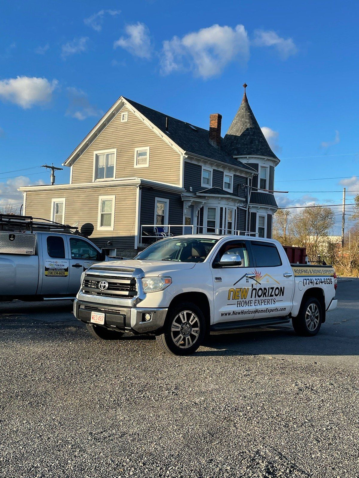 White Toyota truck parked in front of a gray house with a turret, blue sky.