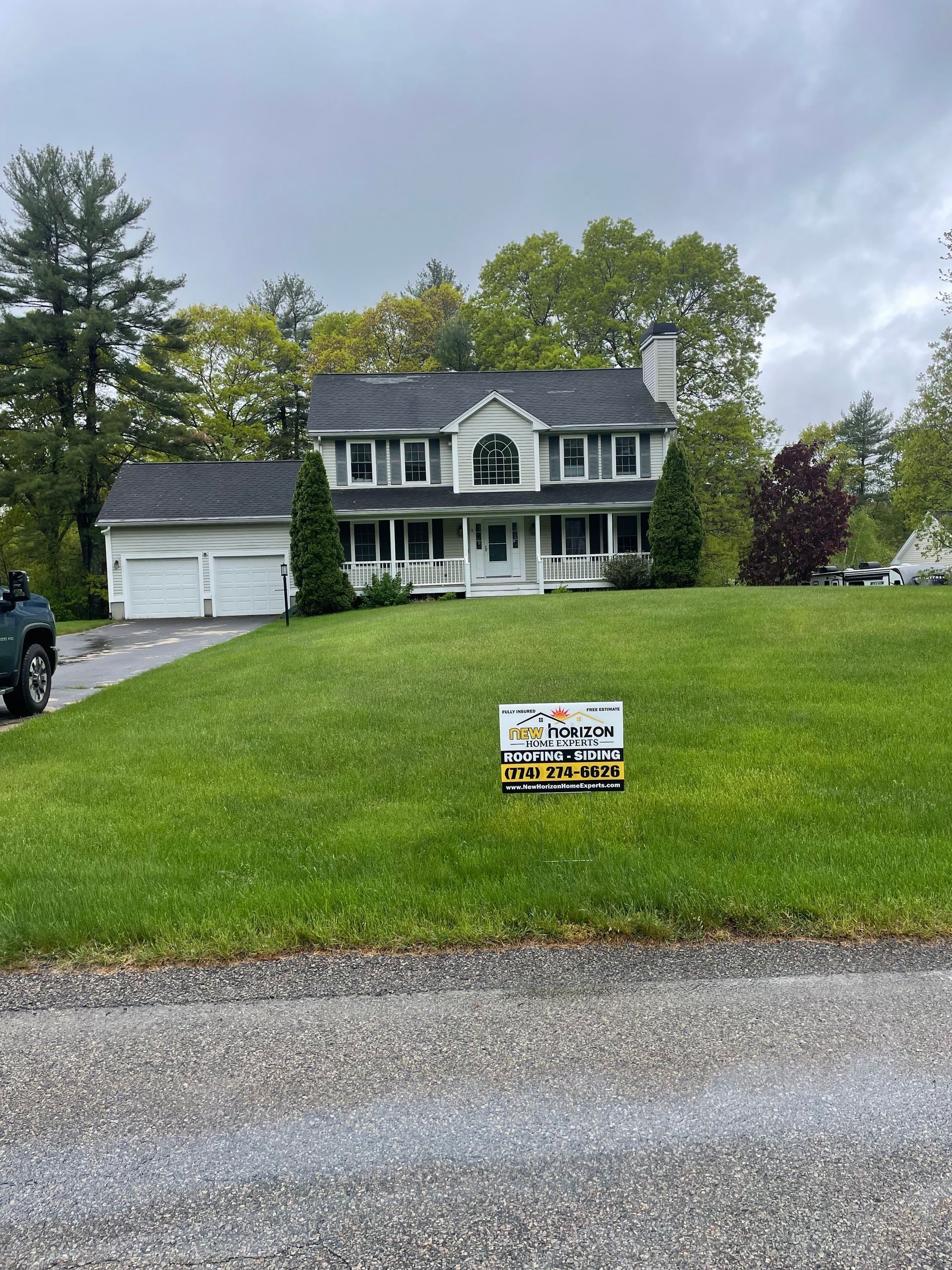 White two-story house with a lawn, driveway, and a sign; cloudy sky.