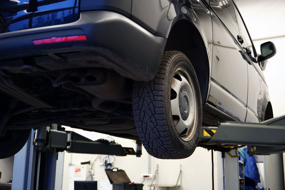 Black van on a vehicle lift in a garage, showcasing the undercarriage and tire.