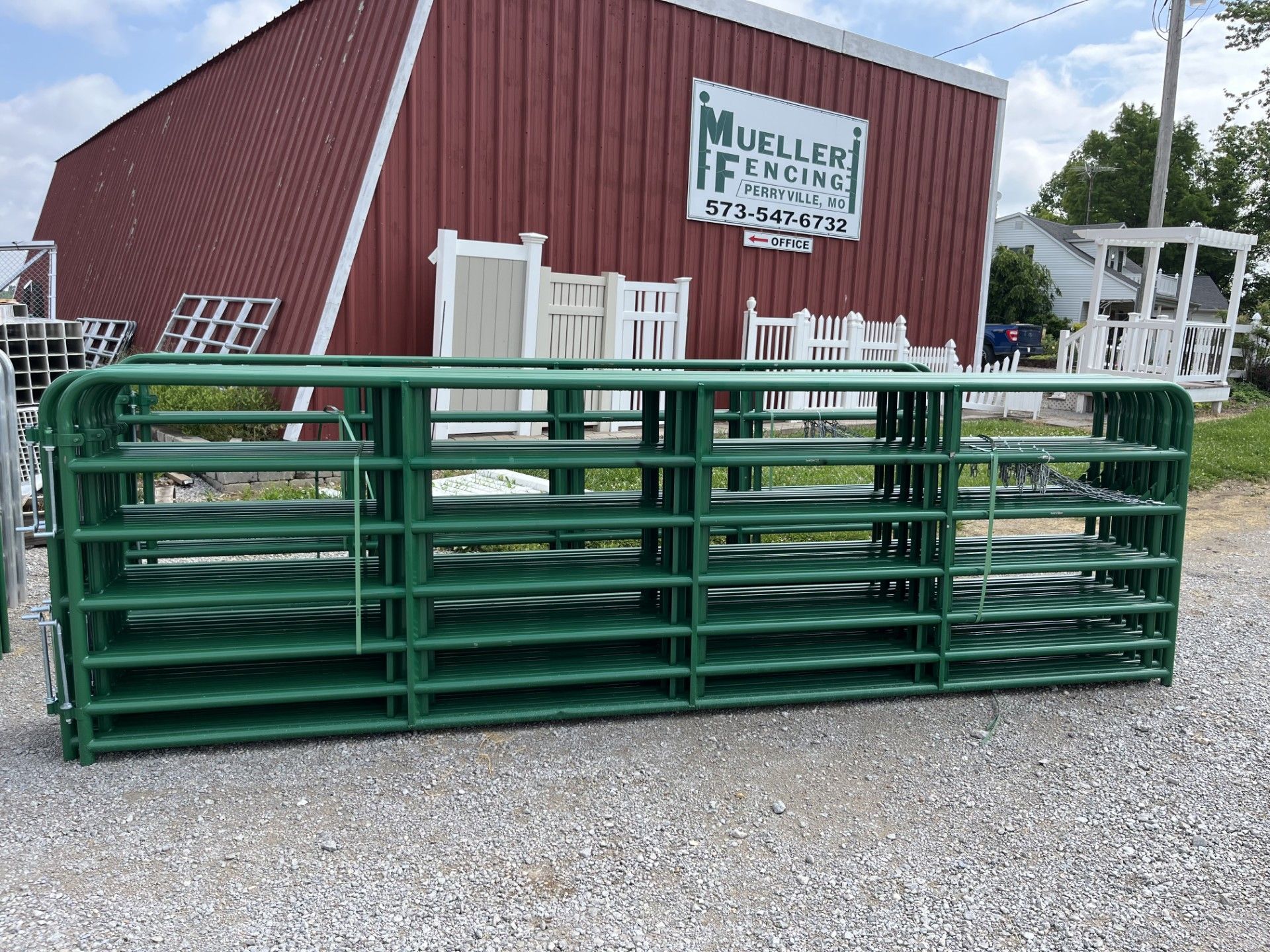 A green fence is sitting in front of a red barn.