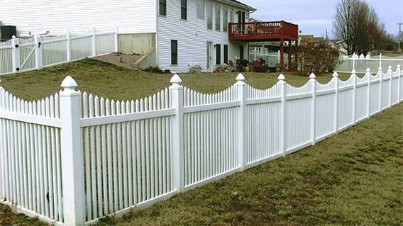 A white fence surrounds a house in a grassy yard.