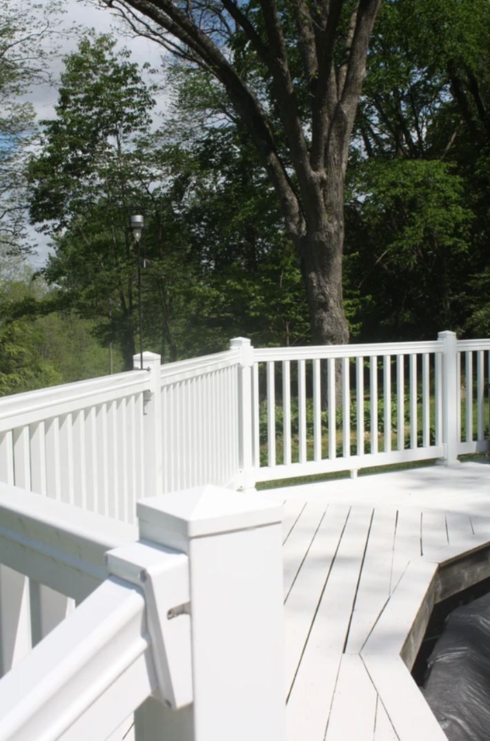 A white fence surrounds a deck with trees in the background