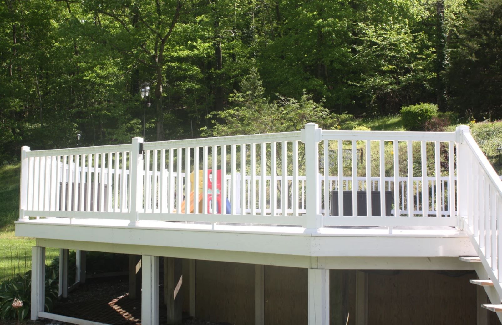 A white deck with a white railing is surrounded by trees