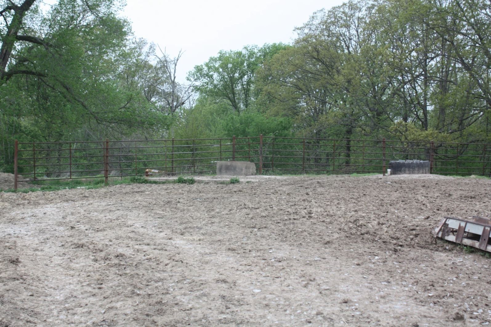A dirt field with a fence and trees in the background