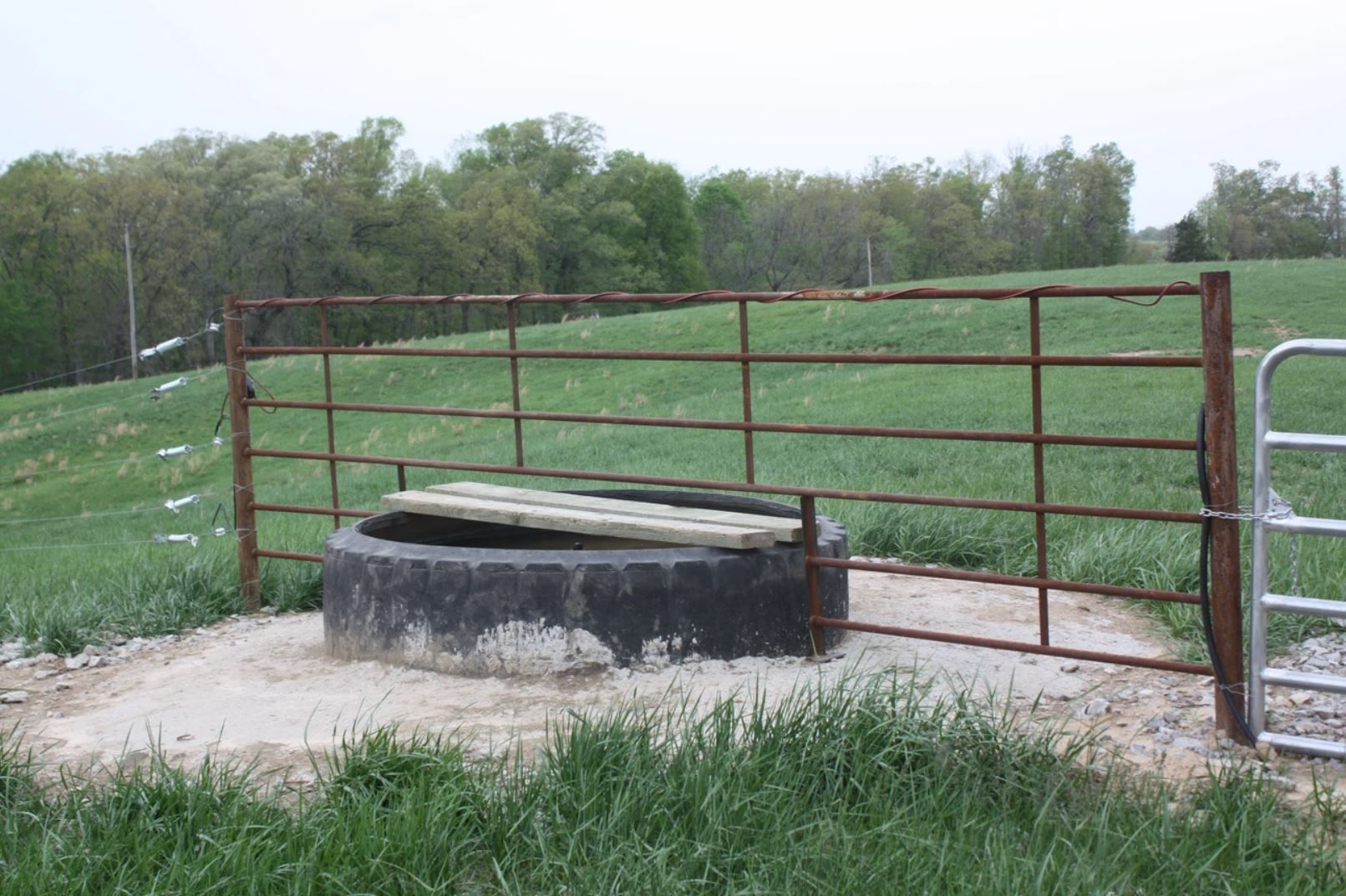A fence surrounds a well in a grassy field