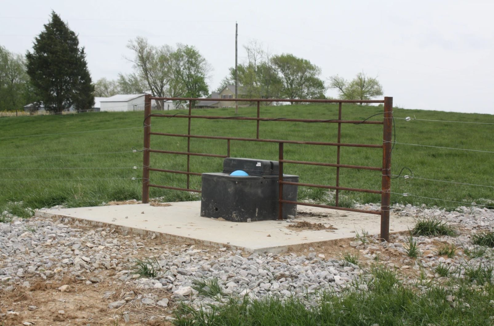 A metal fence surrounds a concrete area in a grassy field