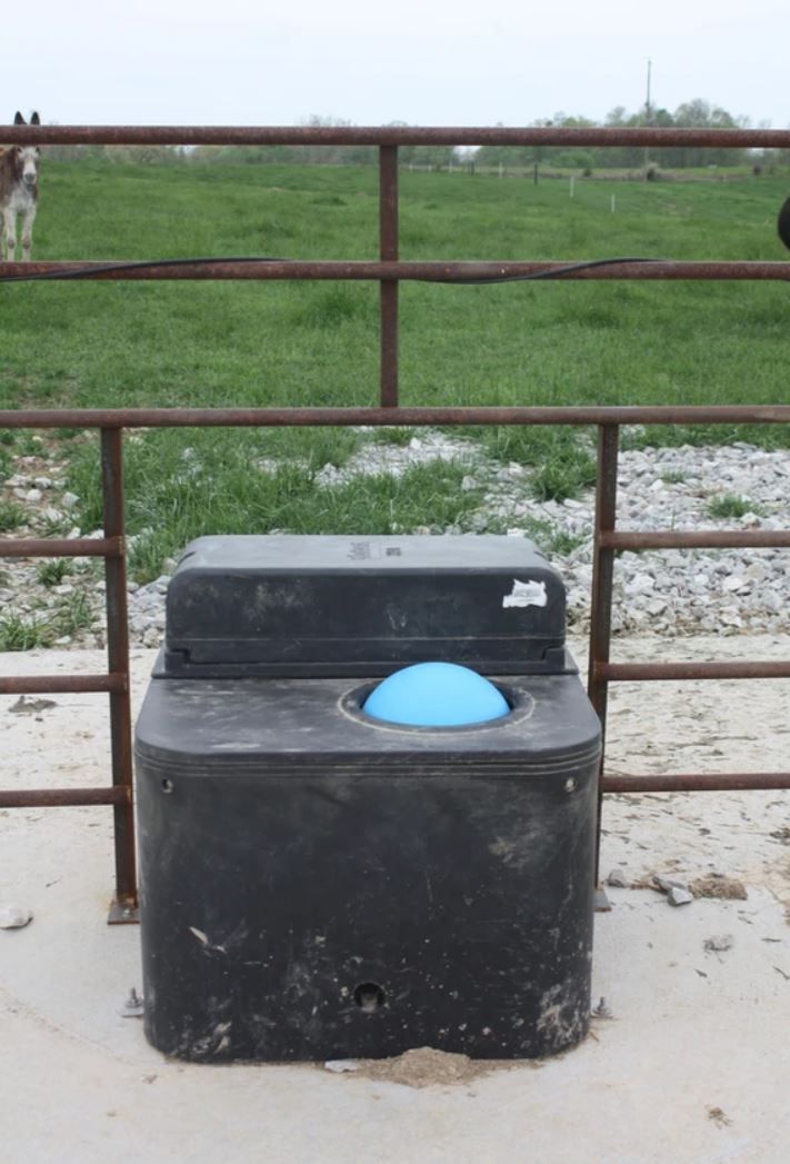 A black container with a blue ball in it is sitting in front of a fence.