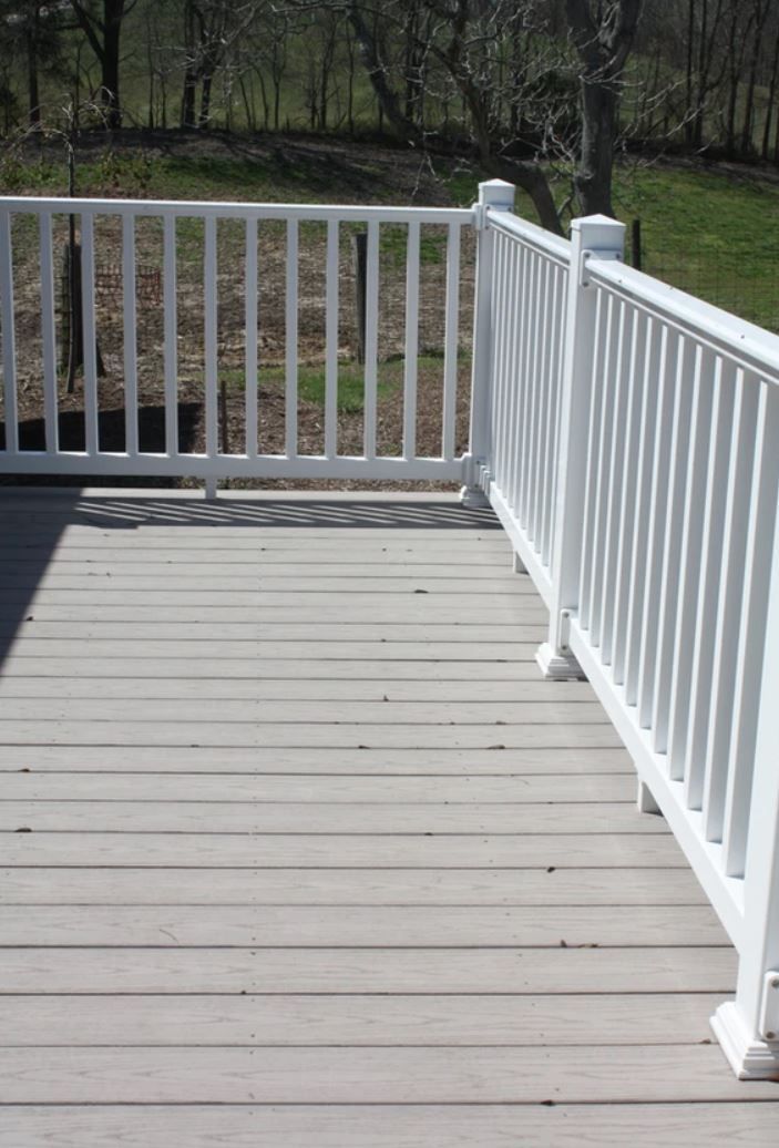 A white railing on a wooden deck with trees in the background