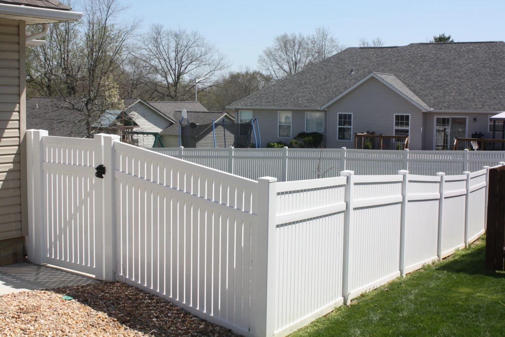 A white fence with a gate in the backyard of a house.