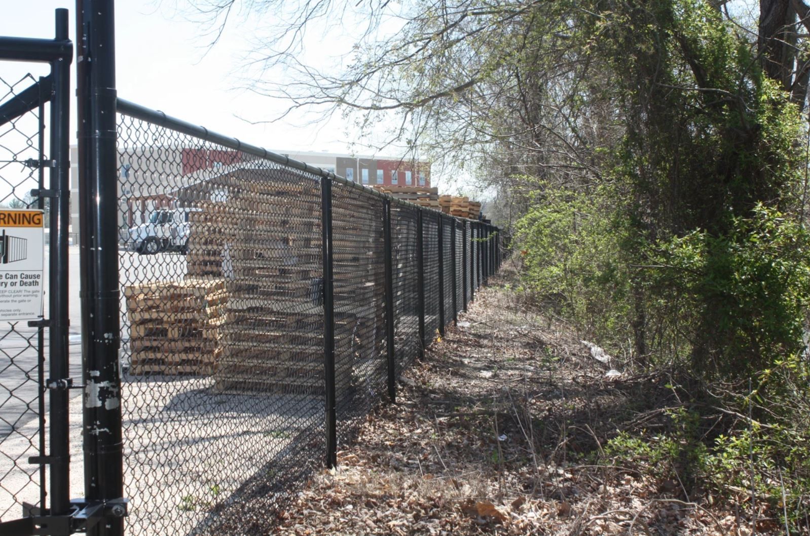 A chain link fence surrounds a lot of wooden pallets