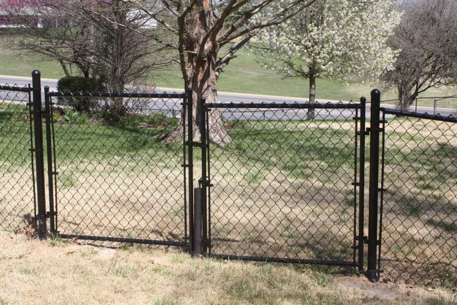 A chain link fence with a gate is surrounded by grass and trees.