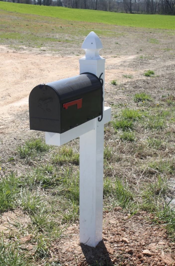 A black mailbox is sitting on a white post in the middle of a field.