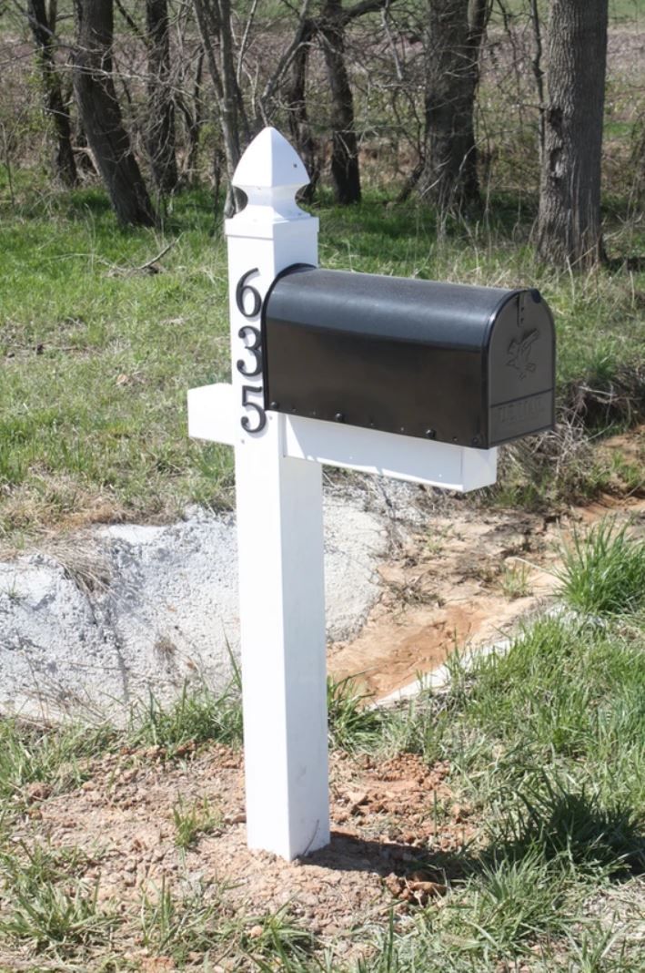 A black mailbox is sitting on top of a white post.