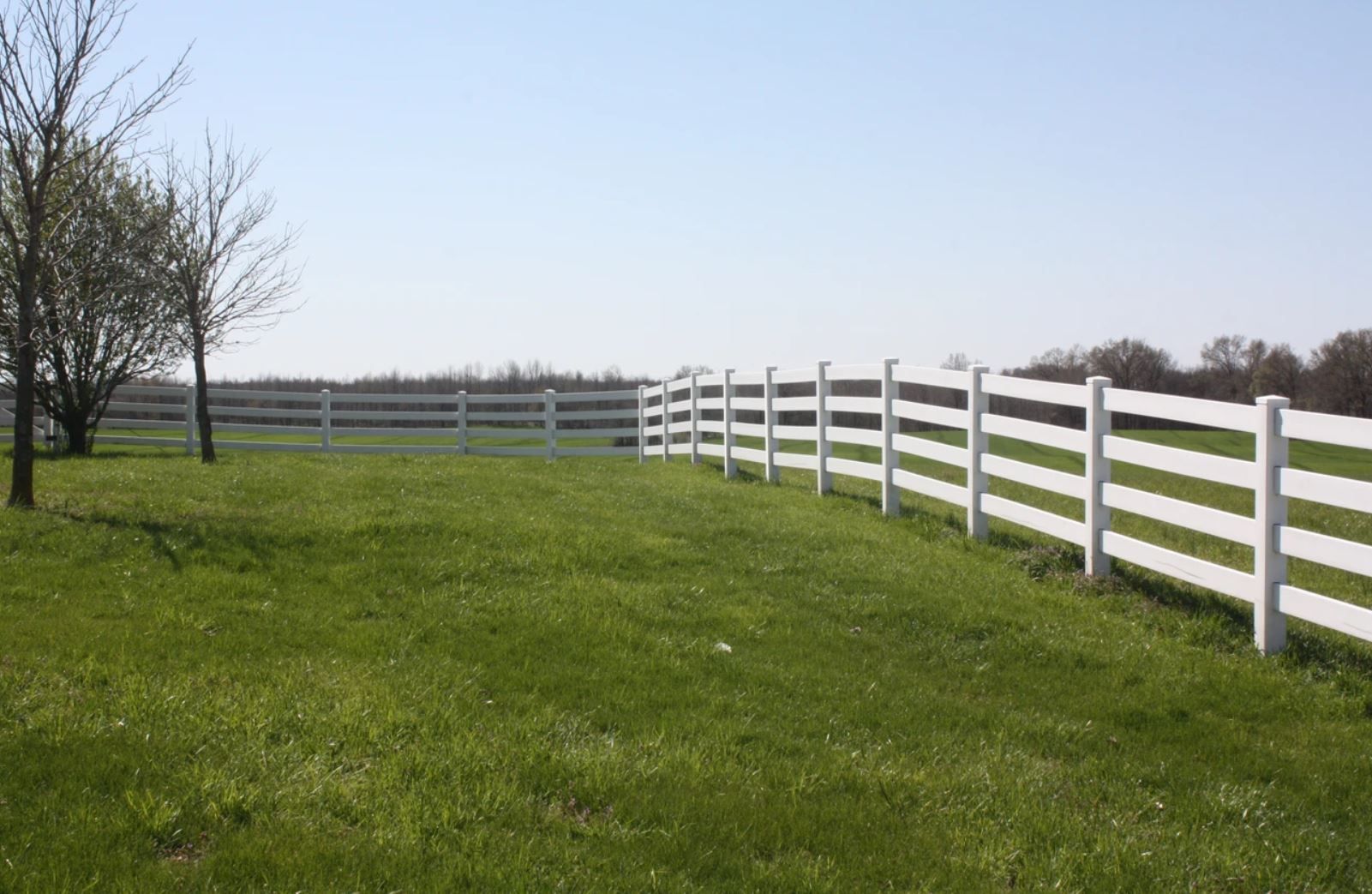 A white fence surrounds a lush green field.