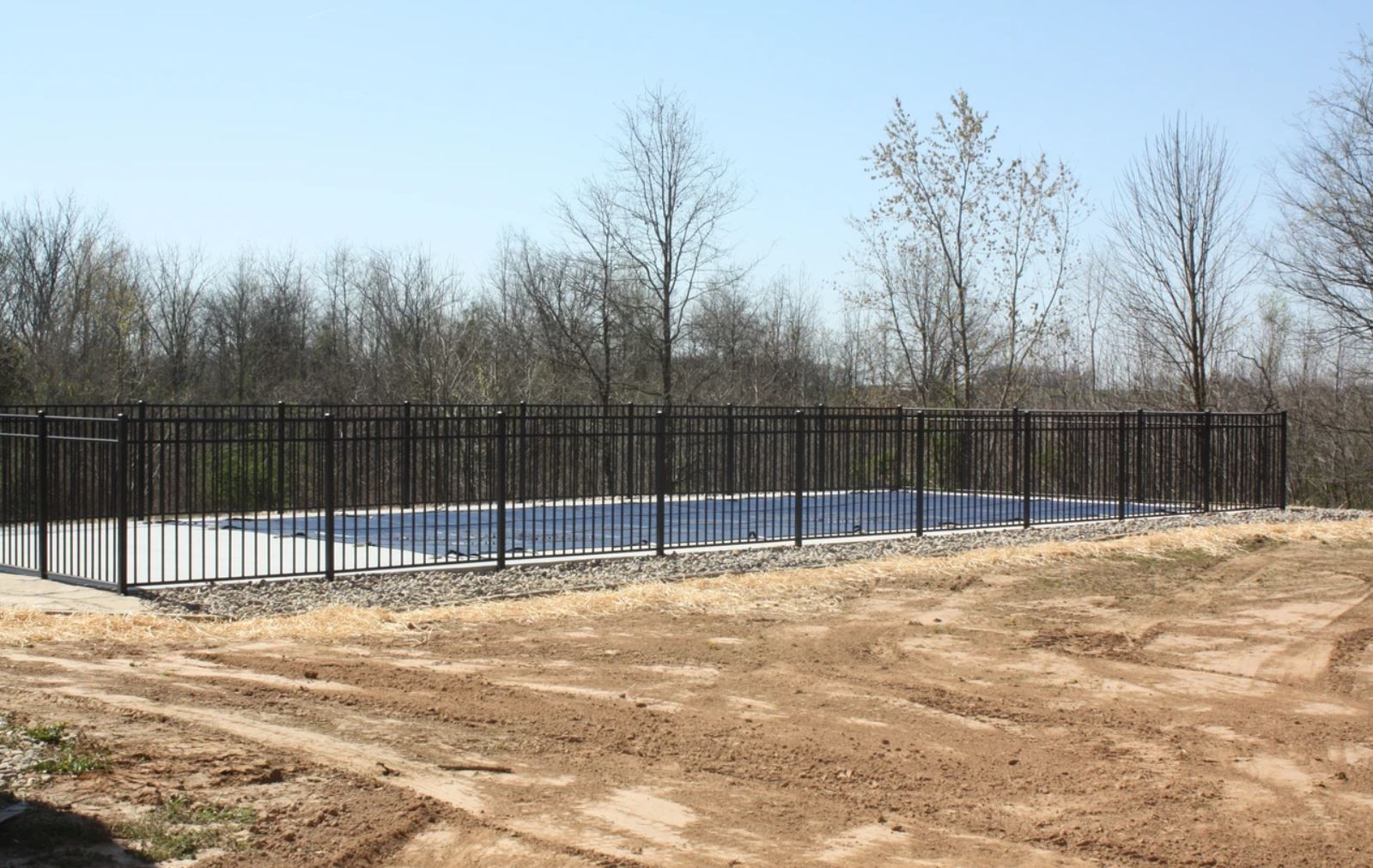 A fence surrounds a swimming pool in a dirt field.